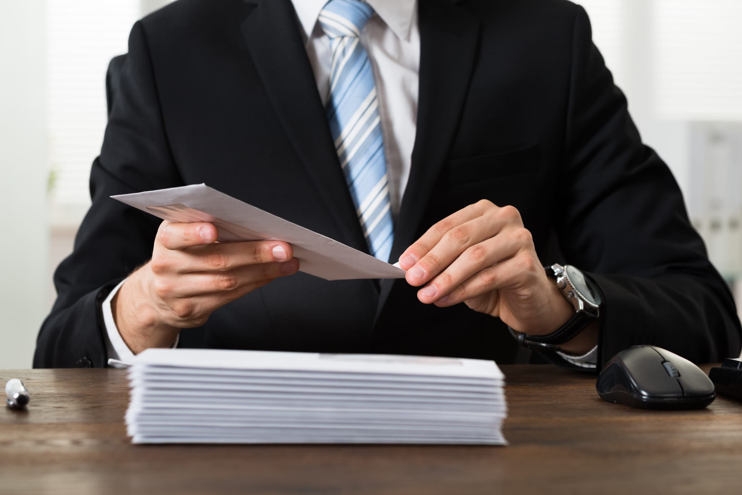 Business professional reading a document at a desk with a stack of papers and a computer mouse.