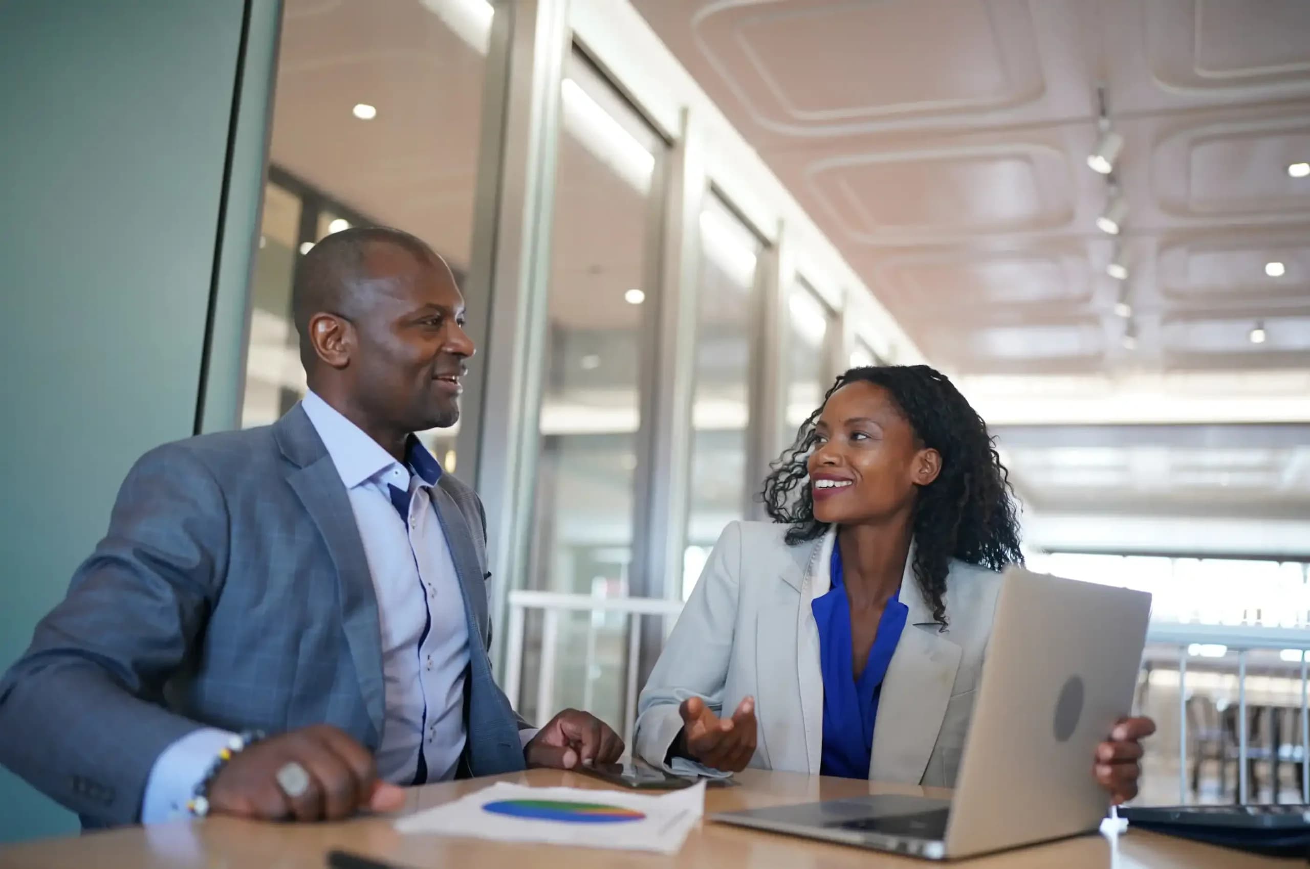 Black businessman and businesswoman having a discussion in an office setting.